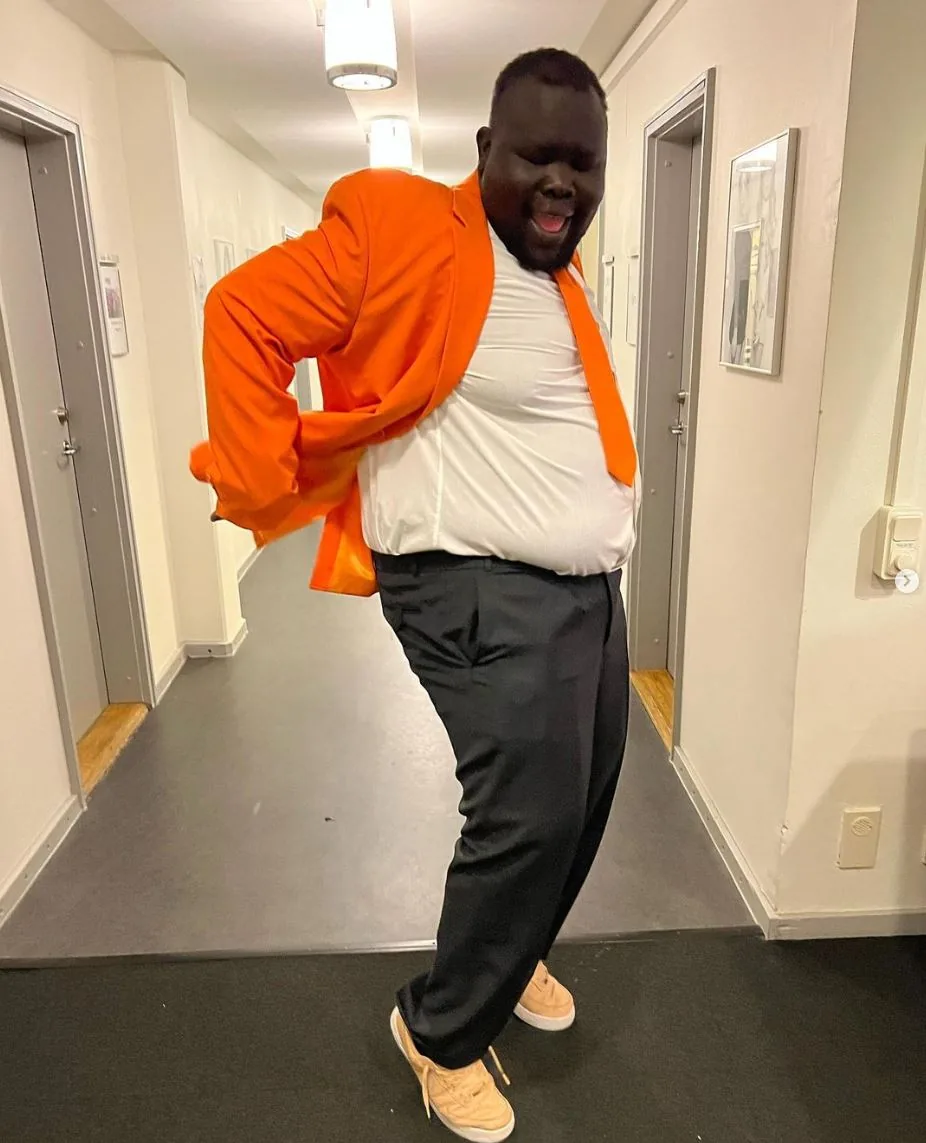 Megic Mike dansar i en korridor i orange kavaj och skjorta
